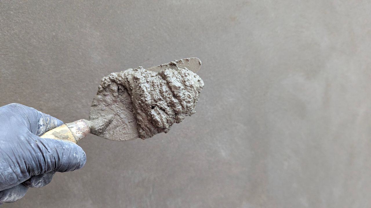 Home Close-up of a hand holding a trowel with cement, perfect for construction themes.